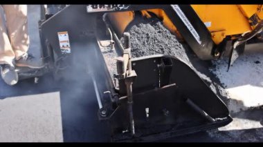 Asfalt işleri asfalt döşeme ile yürütülüyor. Siyah çakıllar işçiler tarafından kürekleniyor.