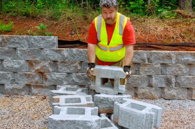 İnşaat işçisi beton blokları kaldırır ve onları istinat duvarlarına yerleştirir..