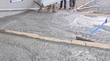 After pouring concrete worker uses trowel to plaster wet concrete cement floor