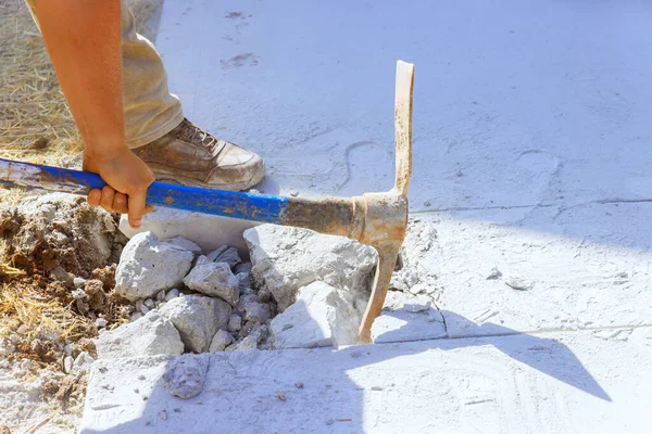 Concrete driveway demolition by worker using pickaxe at construction site