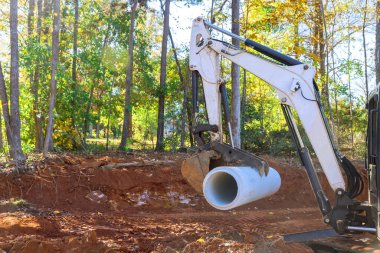 Yeraltı tesisat hazırlama işçisi bir kanalizasyon borusunu beton kaldırmak için traktör kullanıyor