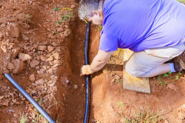 Tesisatçı yer altı için PVC su borusunu kaplayan termal yalıtım köpüğü kullanıyor.
