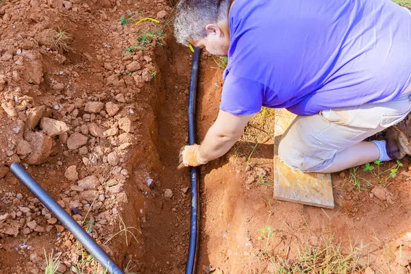 Tesisatçı yer altı için PVC su borusunu kaplayan termal yalıtım köpüğü kullanıyor.