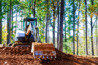 Kazıcı inşaat sahasında çalışıyor. Ev için zemin hazırlama alanı var.