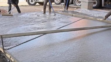 İnşaat alanındaki işçiler durgun beton malayla garaj yolu için beton döşüyorlar.