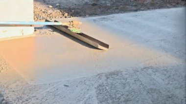 This construction worker is holding a steel trowel and smoothing out the plastering of new sidewalk on freshly laid concrete slab
