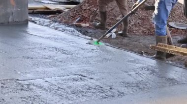 There is worker holding a steel fresno concrete trowel against freshly poured concrete as he smooths the plastering of new sidewalks in construction site