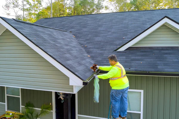 Worker is cleaning clogged roof gutter from dirt, debris fallen leaves to prevent water let rainwater drain