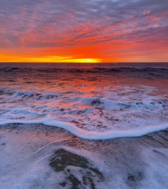 Sabah, okyanus dalgaları dalgalar tarafından kırılırken, güneş okyanus üzerinde yükselir.