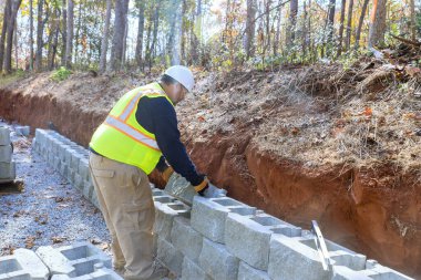 İnşaat işçisi inşaat sırasında beton blokları istinat duvarına monte eder