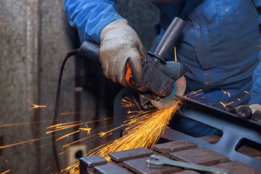 İşçi, endüstriyel fabrikada demir öğütürken aşındırıcı bir disk ile metali keser.