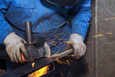 İşçi endüstriyel bir fabrika kıvılcımında aşındırıcı bir disk kullanarak metali keser