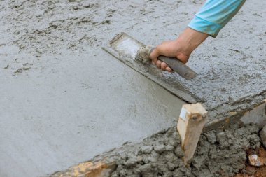 Mason, özel çalışma araçları kullanarak beton kaldırımı ıslak çimentoyla dümdüz ediyor.