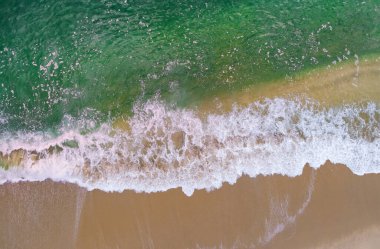 Okyanus yüzeyindeki kumlu kıyı şeridine çarpan dalgaların hava perspektifinden görüntüsü