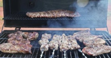Barbekü ızgarasının üzerinde çeşitli sulu etler tüttürülüyor.