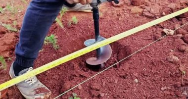 Benzin sondaj makinesinin yardımıyla çit kazmak için toprak kazıyor.