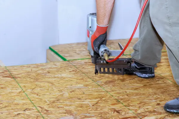 Using an air nail gun to install wooden plywood floors in new home