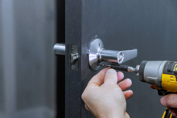 Carpenter uses screwdriver to install lock handles on room door