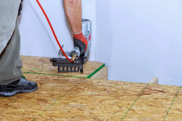 Installing wooden plywood floor in new home using an air nail gun