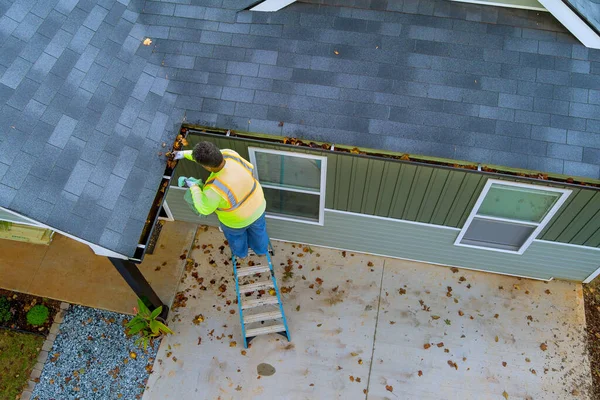 This worker is cleaning out clogged roof gutter drains that have become clogged with dirt, debris, fallen leaves