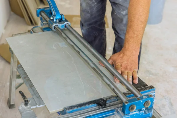 An employee of construction company uses tile cutting hand machine to cut ceramic tiles.