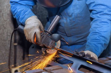 İşçi, endüstriyel bir fabrikada kıvılcım çıkarırken aşındırıcı disk kullanarak metali kesiyor.