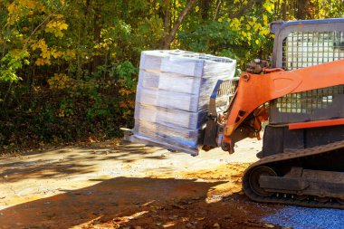 İşçi, duvar tutmak için beton blokları boşaltmak için küçük traktör kullanıyor