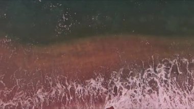 Resimli ortamda kumlu kıyı şeridine çarpan temiz su dalgaları