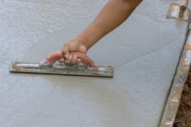 İşçi, özel bir çalışma aracı kullanarak ıslak çimento ile taze beton kaldırımı düzleştiriyor