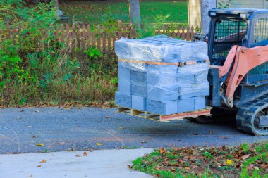 Duvarları muhafaza etmek için beton bloklar küçük traktör kullanan işçiler tarafından paletlerden kaldırılır