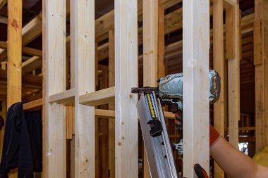 İnşaatçı, ev iskeletine tahta kirişleri güvence altına almak için bir hava çekici kullanıyor.