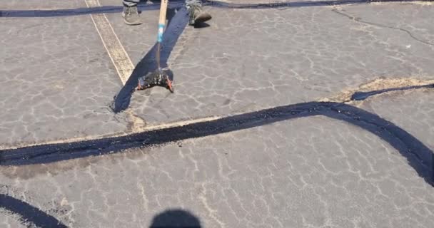 노동자는 아스팔트 균열을 덧대고 유화액을 사용하여 밀봉하고 도로의 표면을 복원합니다 — 비디오