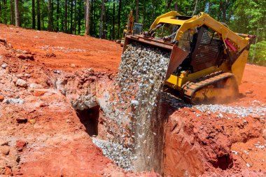 Bir kazıcı kovasına yerleştirilmiş patinaj direksiyonlu çakıl taşları boşaltılıyor