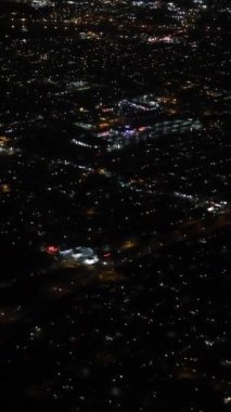 Gece gökyüzü şehrin üzerinde uçan bir uçakla aydınlanır. dikey video