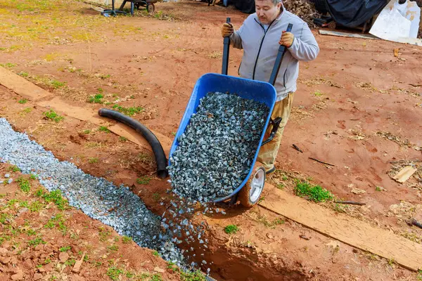 stock image Crushed stone is fills into drainage pipe from wheelbarrow by worker