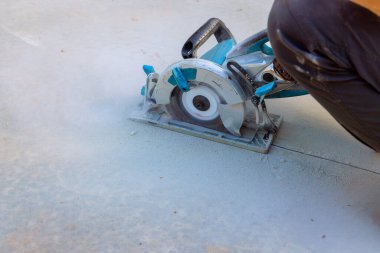 Kesme makinesi öğütücüsünü kullanan inşaat işçileri, döküldükten sonra beton temelleri kesiyor