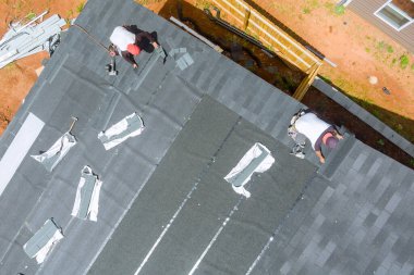 Çatı müteahhidi çatıdaki eve yeni asfalt kiremitleri yerleştirmek için hava çivi tabancası kullanıyor.
