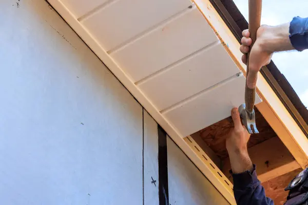 stock image Worker installs plastic vinyl soffit at rooftop corner of rafters house