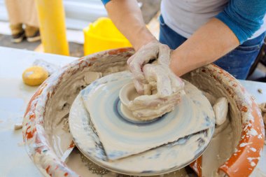Bir sanatçı çömlekçi tekerleği kullanarak ıslak ellerle kil tabaklar yapar.
