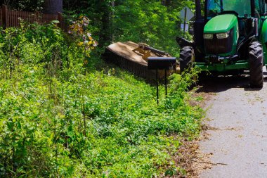 Çim biçme makinesiyle donatılmış belediye hizmet traktörü ile yolun her iki tarafında da çim dalları kesilmiş.