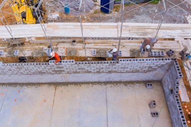 İnşaat iskelesinde çalışan Mason, beton bloklarla beton duvar inşa ediyor.