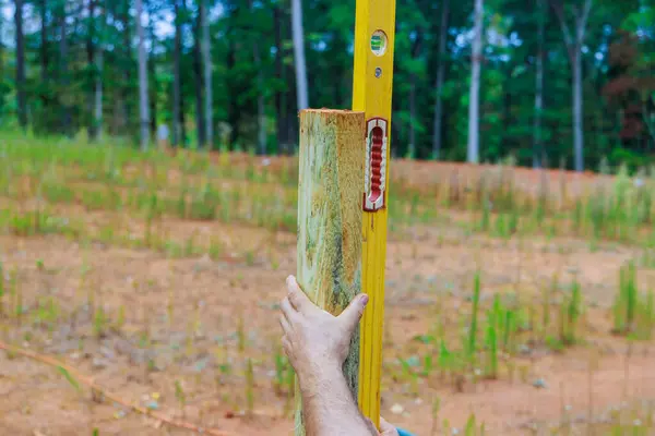 stock image Man building wooden fence in backyard checking posts with level