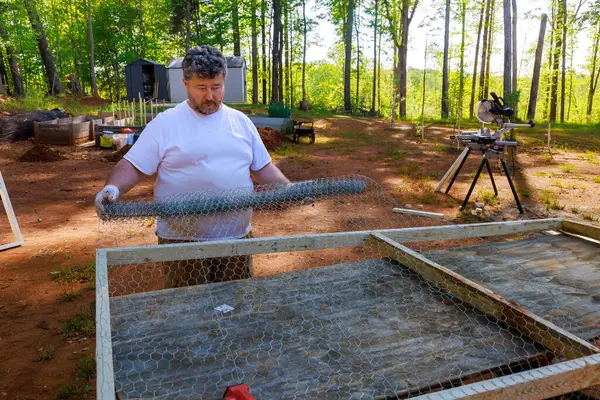 stock image Farmer constructs an outdoor chicken coop using metal mesh