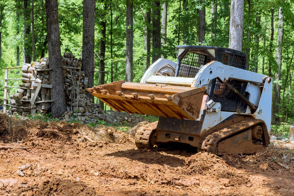 Во время земляных работ трактор выравнивает землю в лесу ведром