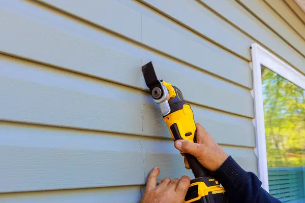 stock image As part of reconstruction of house, multi tool is used to remove damaged vinyl siding