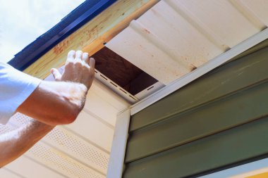 Bir çalışan yeni evin ön tavanına vinil soffit plastik paneller yerleştiriyor