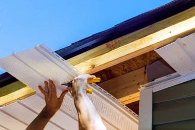 Yeni evin ön tavanına bir çalışan tarafından plastik soffit plastik paneller yerleştiriliyor.
