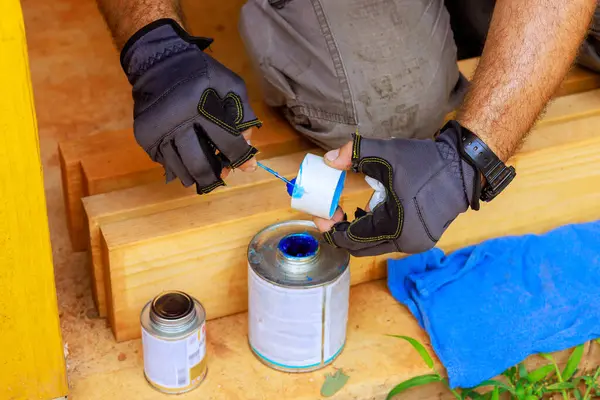 Tesisatçı tarafından su hattı döşemek için plastik PVC borulara yapıştırıcı yerleştiriliyor