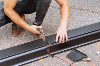 Makinedeki alüminyum yağmur oluklarını büktükten sonra, işçiler bunları gerekli boyuta kadar makasla kesiyor.