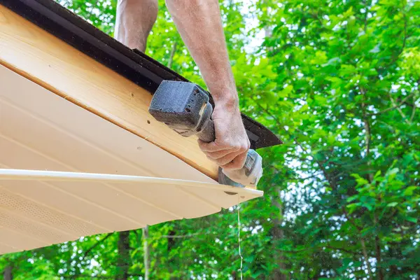 stock image Cutting off existing vinyl soffit plastic panels on new house facade ceiling to specific size